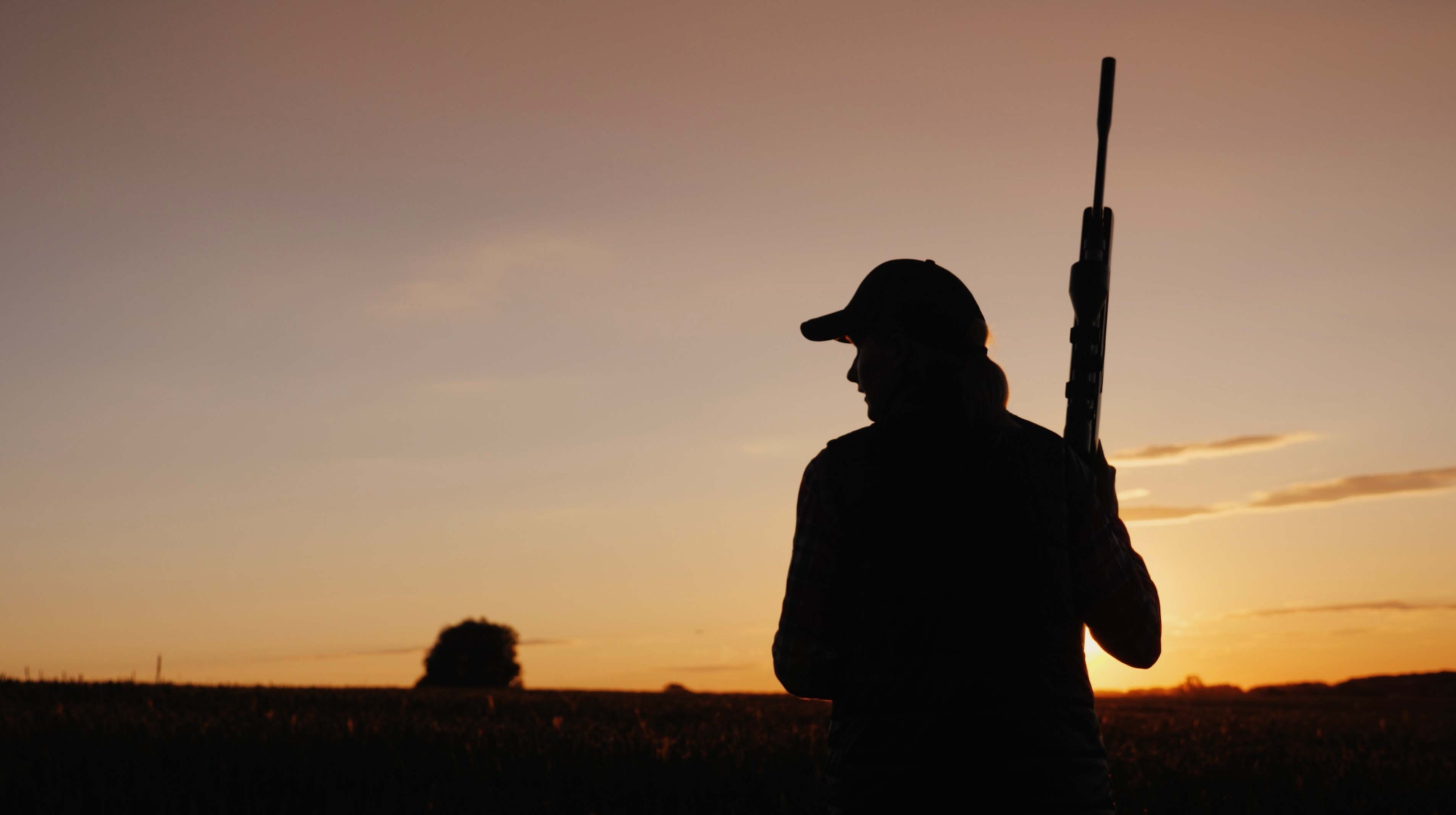 Kvinna med vapen, som går genom en åker i en solnedgång.